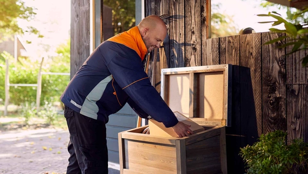 Pakketbezorger stopt een pakket in een opbergbox in een tuin