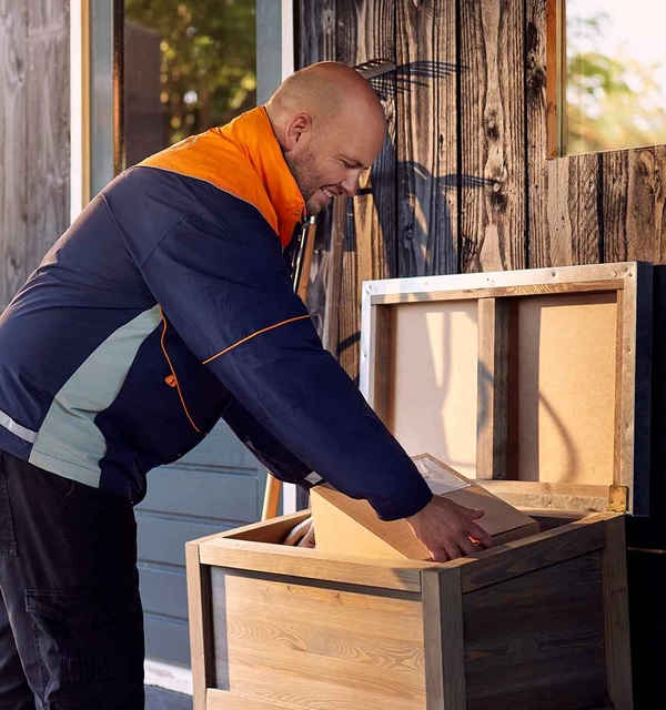 Pakketbezorger stopt een pakket in een opbergbox in een tuin